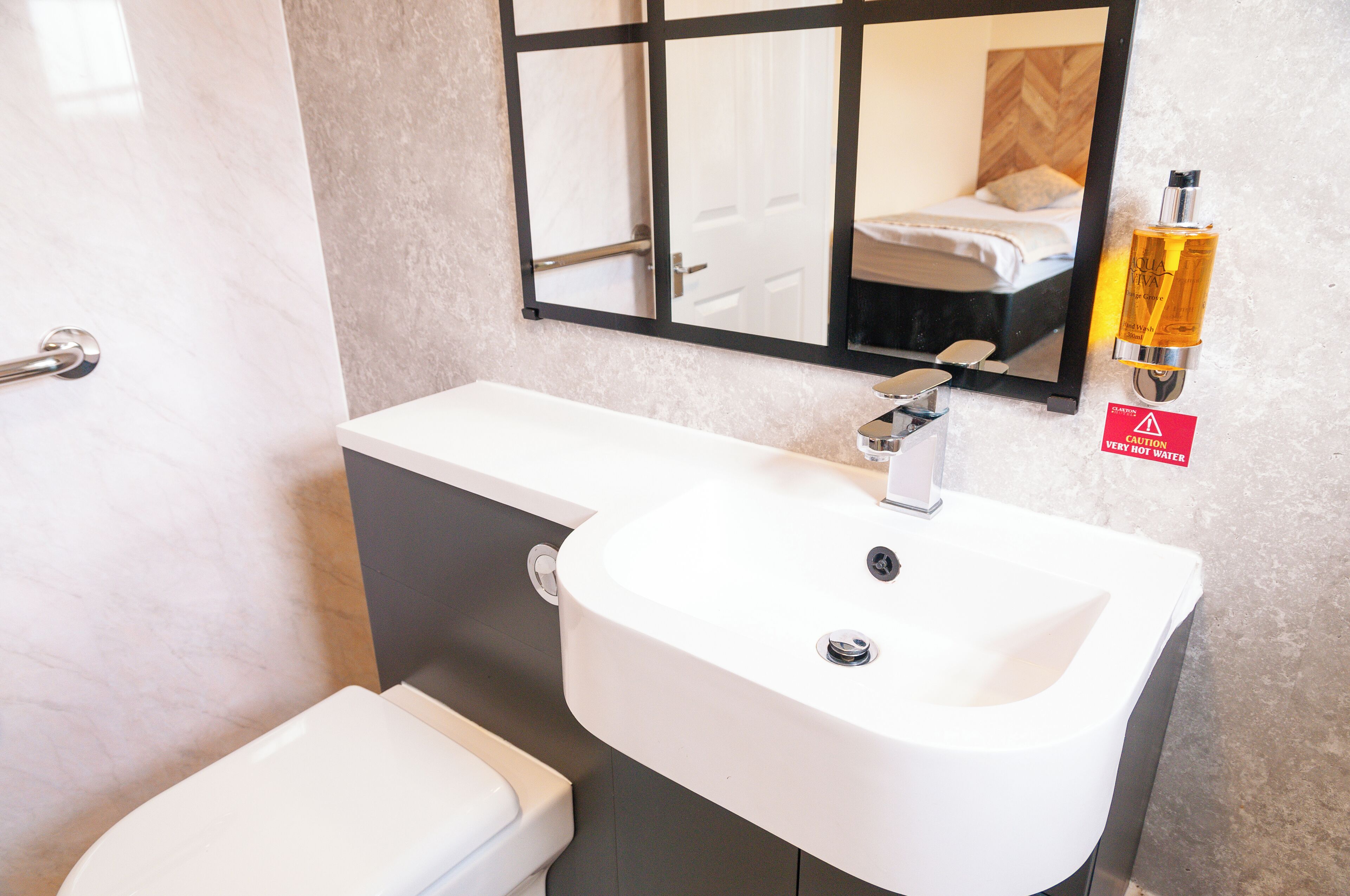 Een badkamer met een wit wastafel, een spiegel en een toilet. Er hangt een waarschuwingsbord aan de muur.