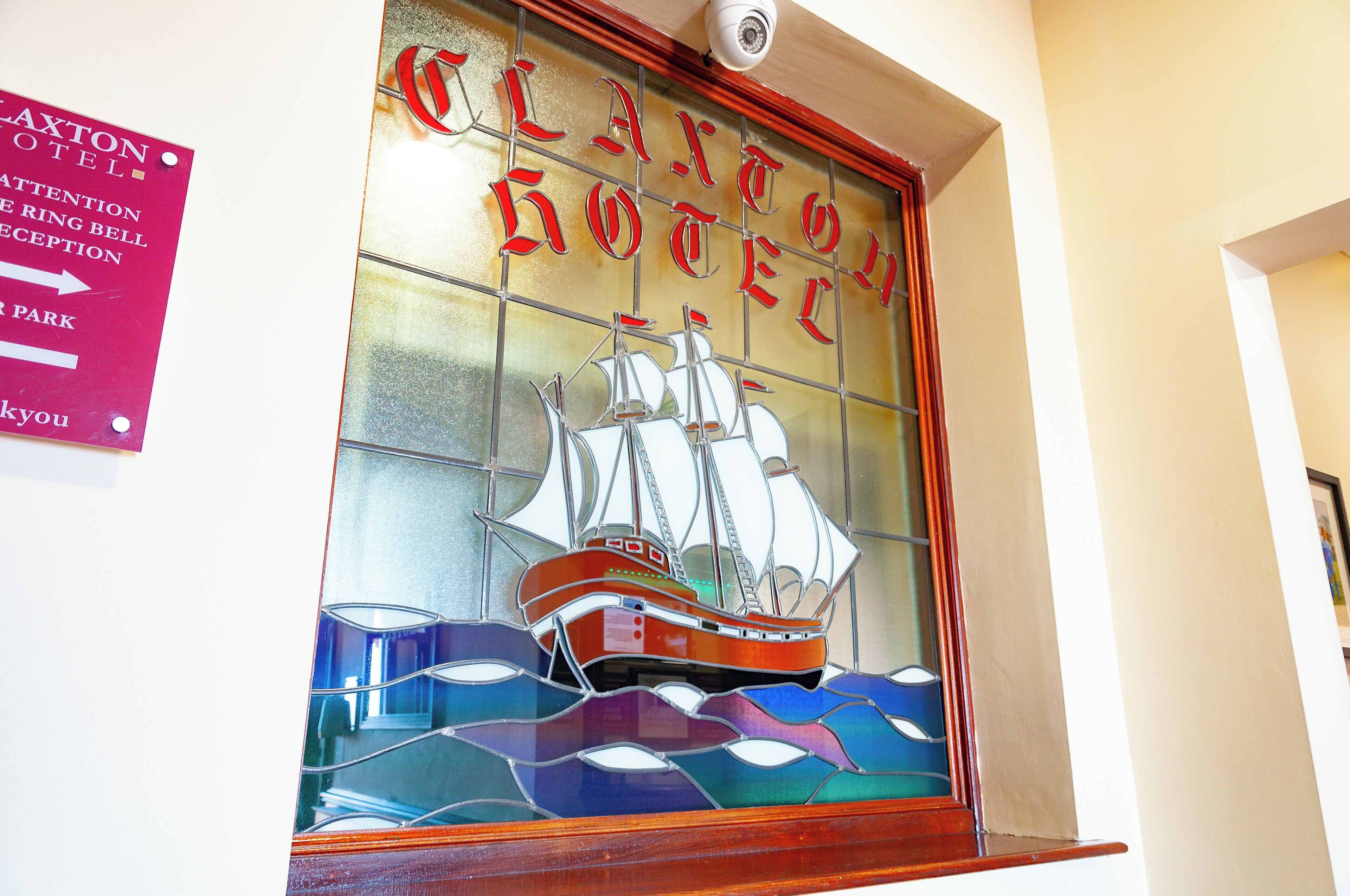 A stained glass window with a ship design, a sign for the Laxton Hotel, and a directional sign for the parking area.