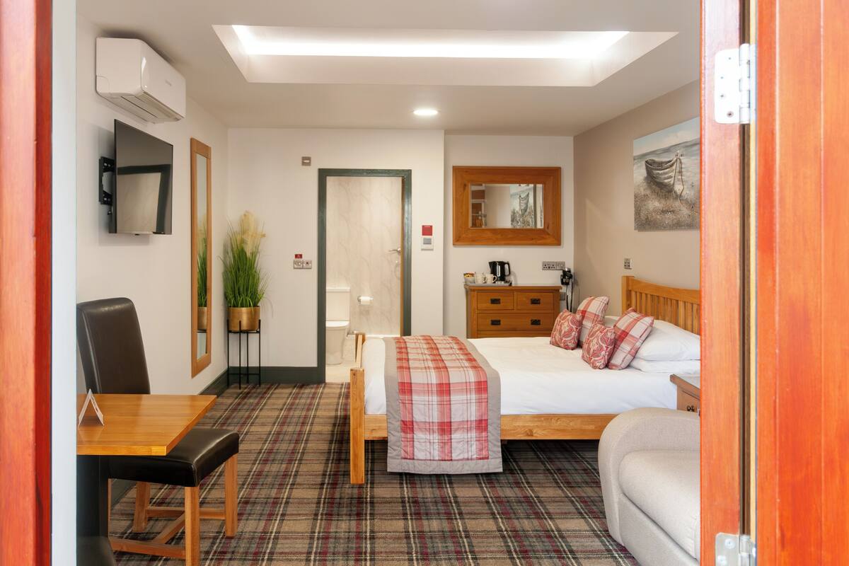 Une chambre d’hôtel équipée d’un lit, d’un bureau, d’une chaise, d’une commode et d’un téléviseur fixé au mur.
