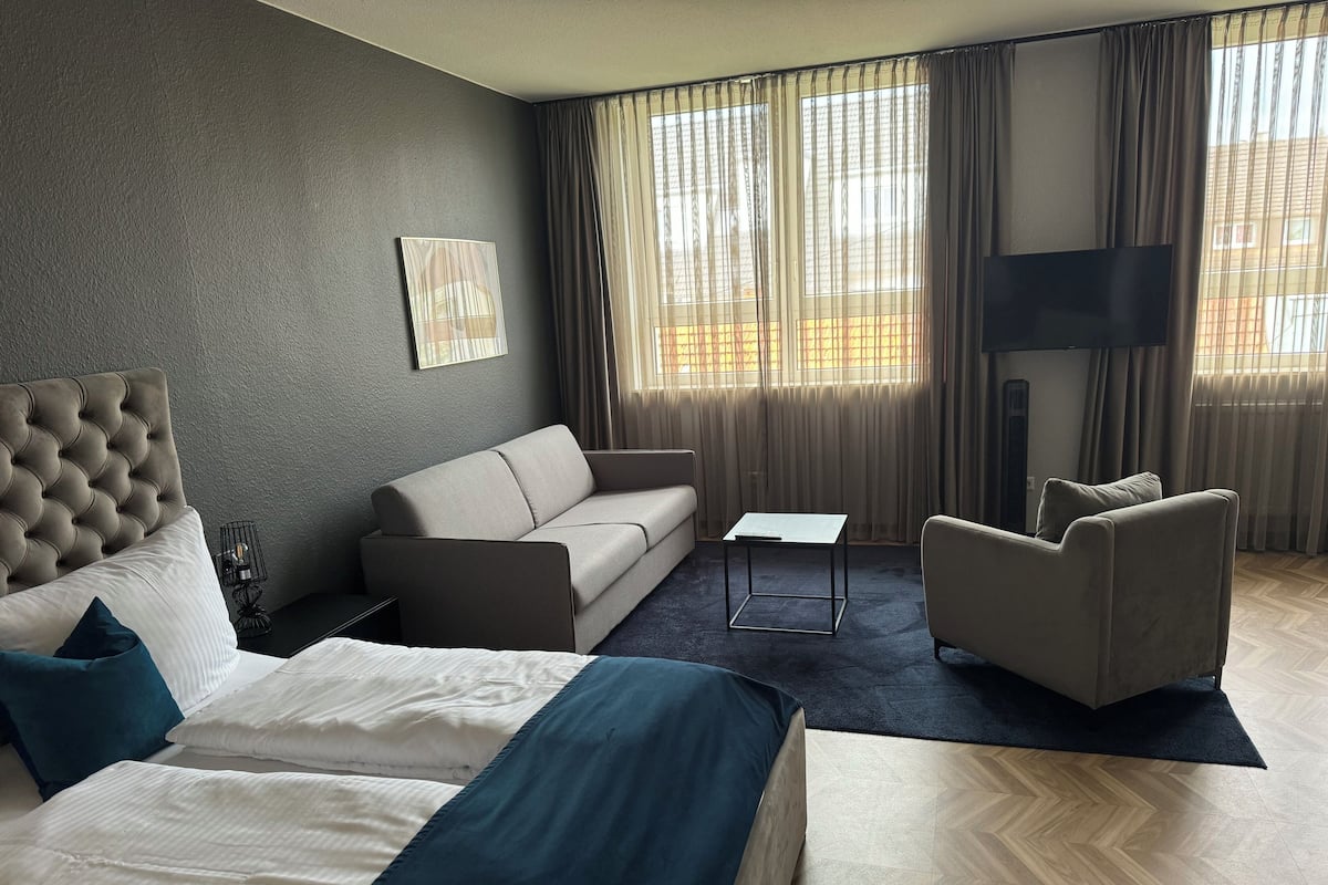 A modern hotel room with a large bed, a sofa, a chair, and a small table.