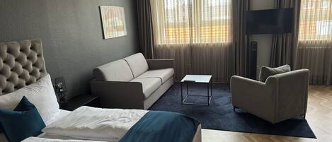 A modern hotel room with a large bed, a sofa, a chair, and a small table.