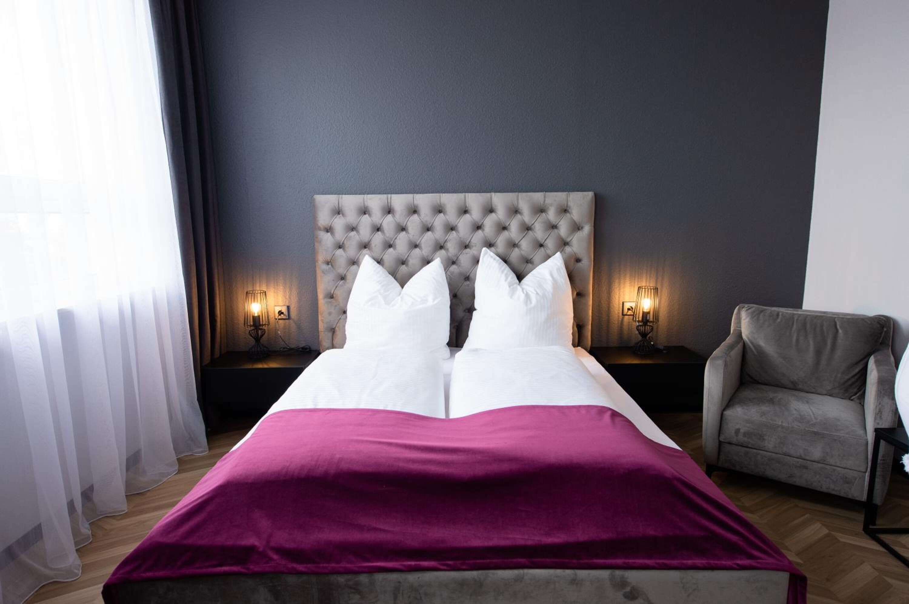 A neatly made bed with white and pink bedding, a tufted headboard, and two bedside lamps.