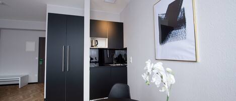 A modern room with a dining table, a black cabinet, a kitchen area, and a framed picture on the wall.
