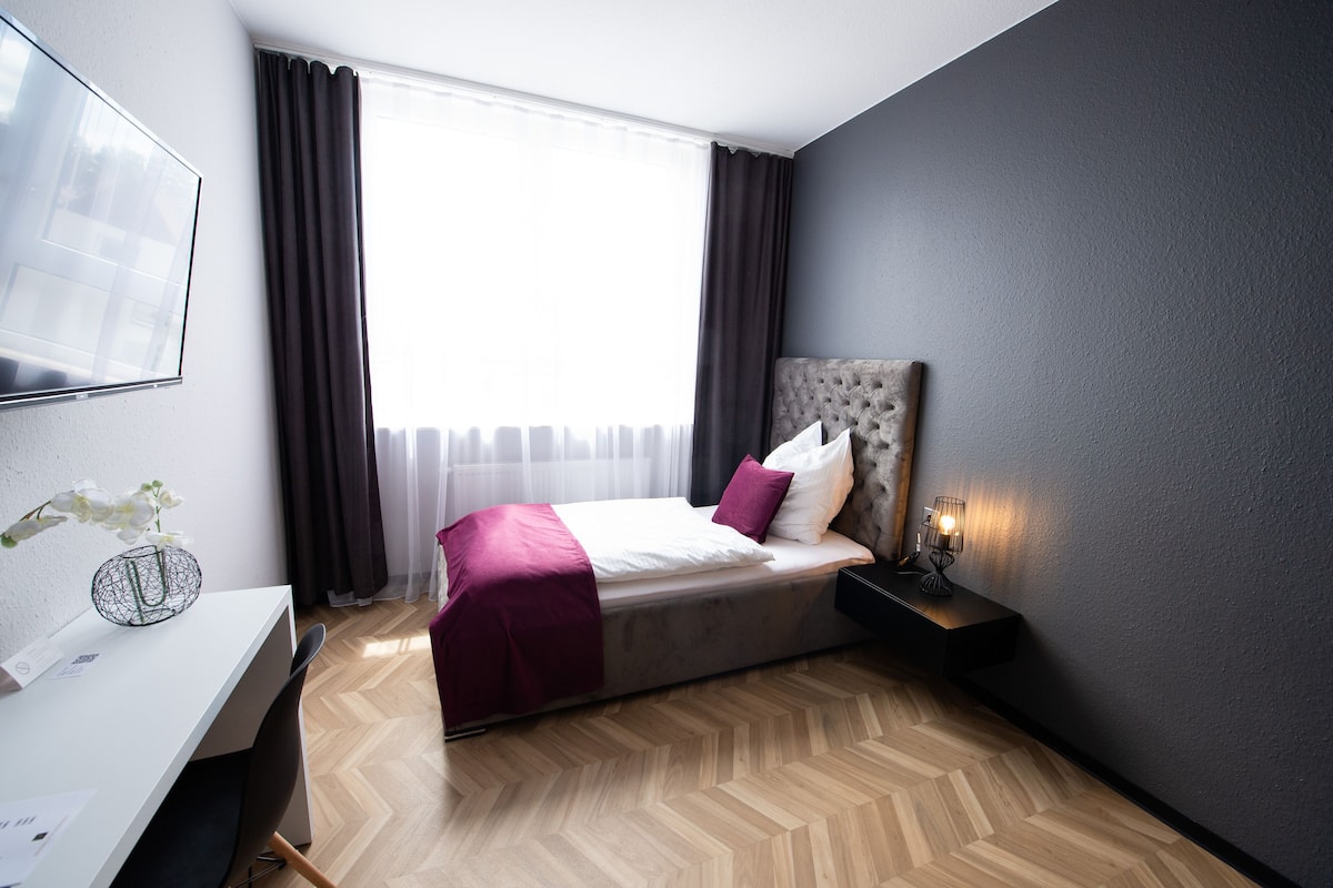 A modern hotel room with a large bed, a desk, and a window with curtains.