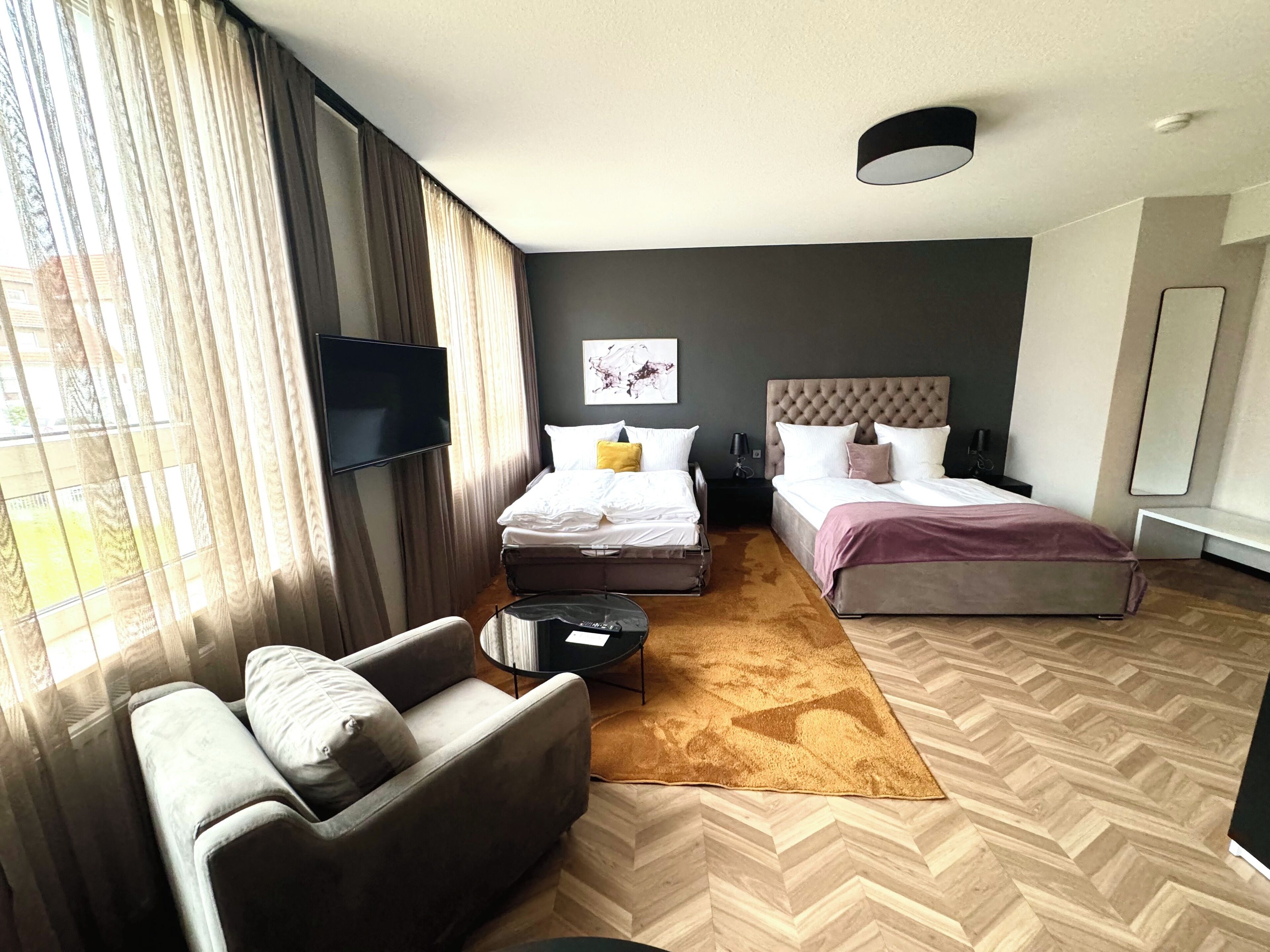 A modern hotel room with a large bed, a sofa, a TV, and a desk.