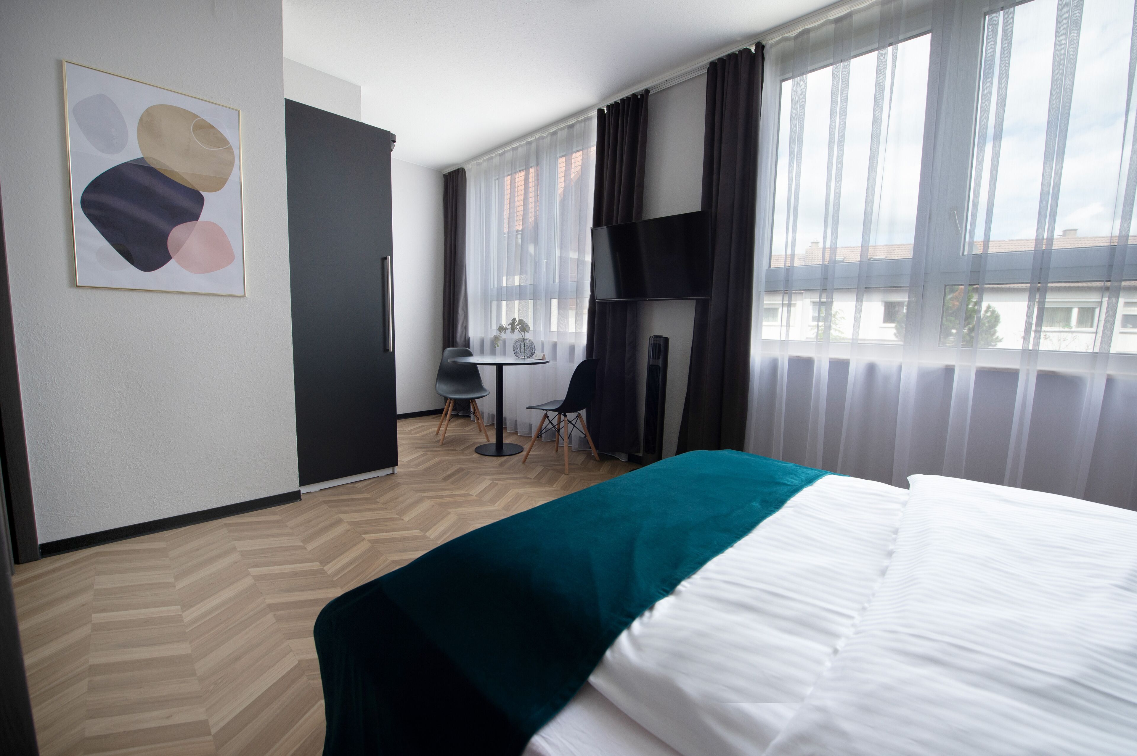 Une chambre d’hôtel avec un lit, un bureau, une chaise, une télévision et une fenêtre avec des rideaux.