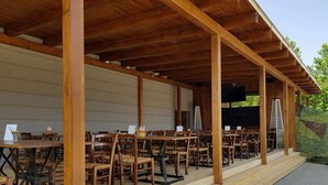 An outdoor wooden pavilion with multiple tables and chairs, a brick pathway, and a large tree trunk to the right. - Hotel Chmelnice (Napajedla)