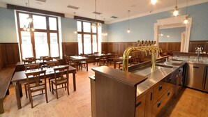 A restaurant with wooden tables and chairs, a bar area with a stainless steel sink, and large windows allowing natural light. - Hotel Chmelnice (Napajedla)
