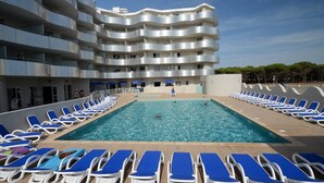 Una piscina con tumbonas y un edificio de varios pisos con balcones.