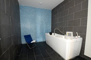 A bathroom with a white bathtub, a blue chair, and a tiled wall.