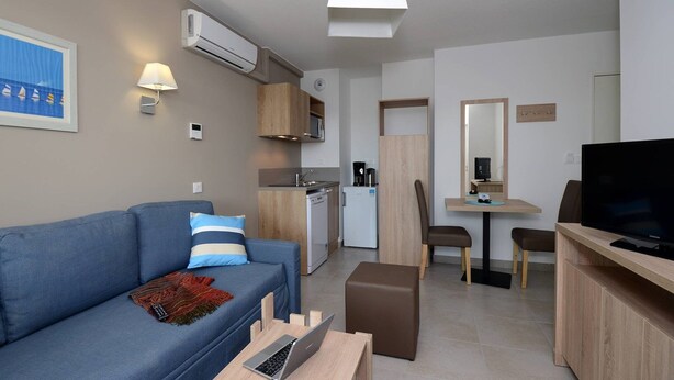 En kompakt bolig med sofa, spiseplads, tekøkken og TV.