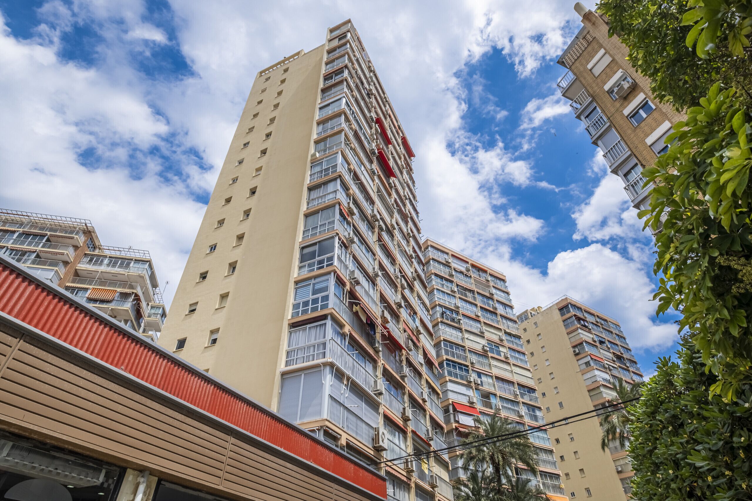 Un edificio de gran altura con múltiples balcones y ventanas, rodeado de otros edificios y árboles.