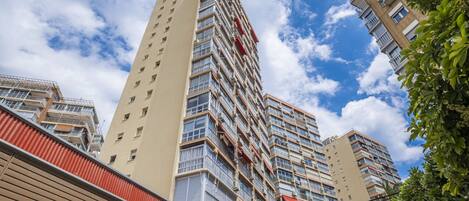 Un edificio de gran altura con múltiples balcones y ventanas, rodeado de otros edificios y árboles.