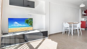 Una sala moderna con un televisor de pantalla plana, un comedor con sillas blancas y una cocina con armarios rojos.