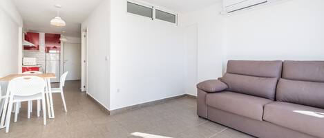 A modern living space with a brown sofa, a dining table with chairs, and a kitchen area in the background.