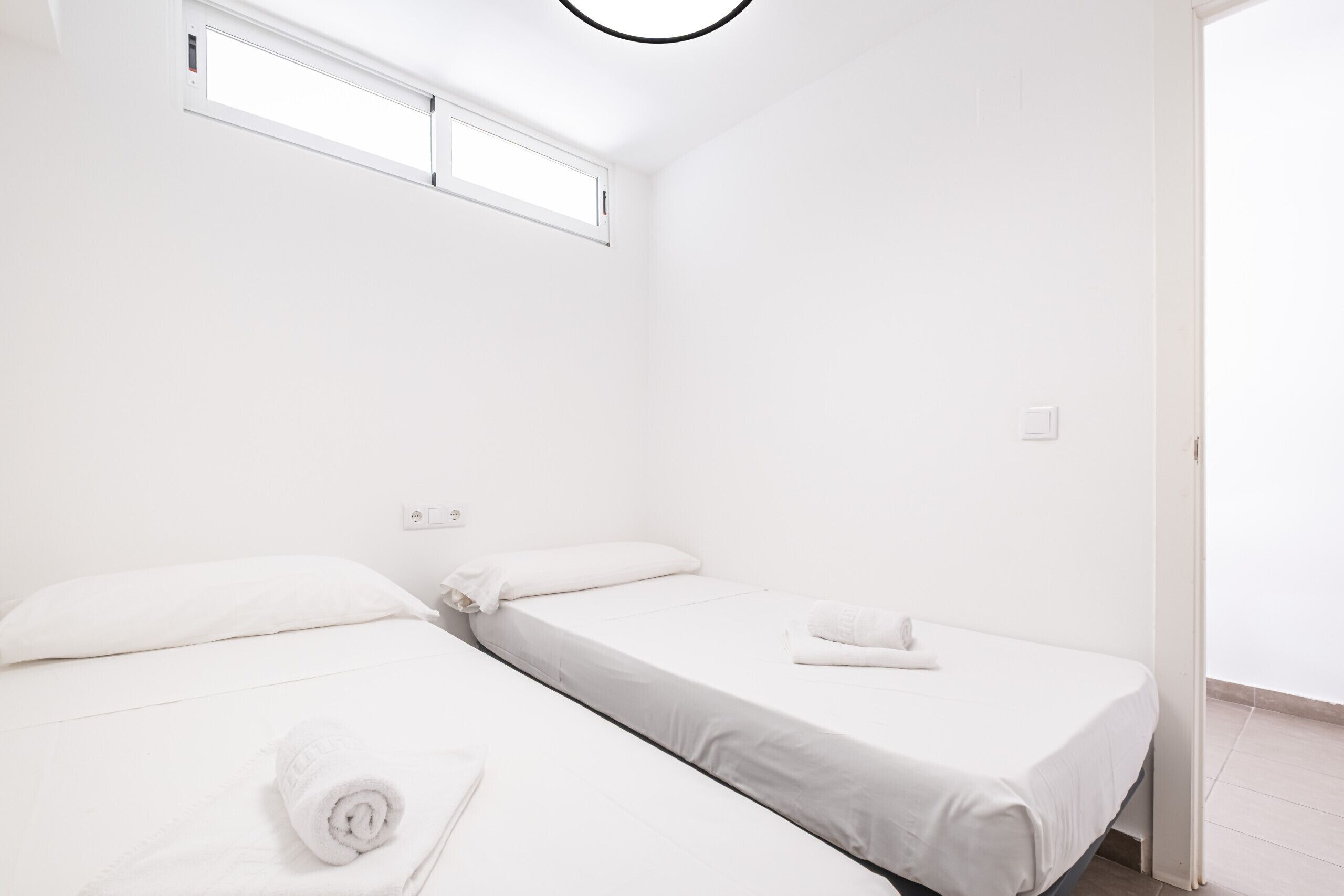 Une petite pièce blanche, avec deux lits simples, une fenêtre et une porte.