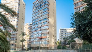 Un edificio residencial alto con varios balcones, un patio cercado y abundante vegetación.