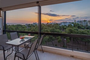 A balcony with a table and chairs, overlooking a cityscape during sunset.
