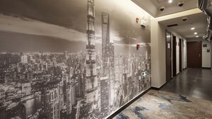 Un pasillo con un mural de paisaje urbano, una alfombra estampada y un techo moderno con iluminación empotrada y detectores de humo.