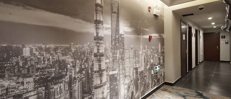 A hallway with a cityscape mural, a patterned carpet, and a modern ceiling with recessed lighting and smoke detectors.