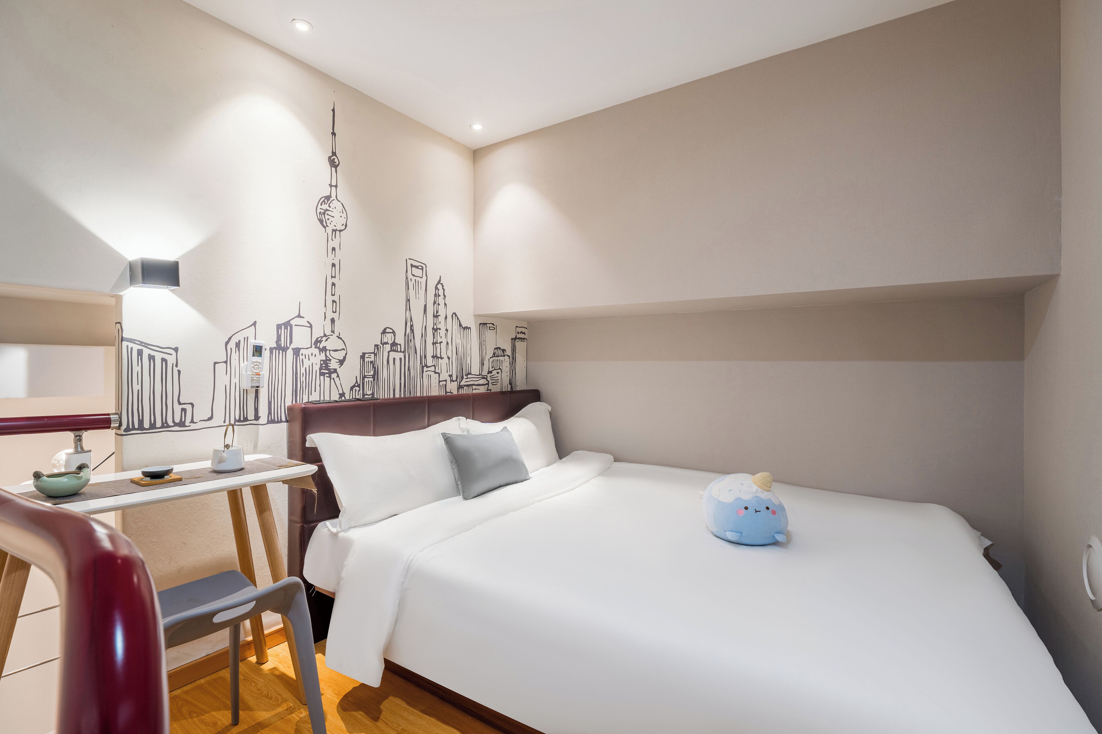 A hotel room with a bed, a desk, and a chair. There is a wall mural of a city skyline.