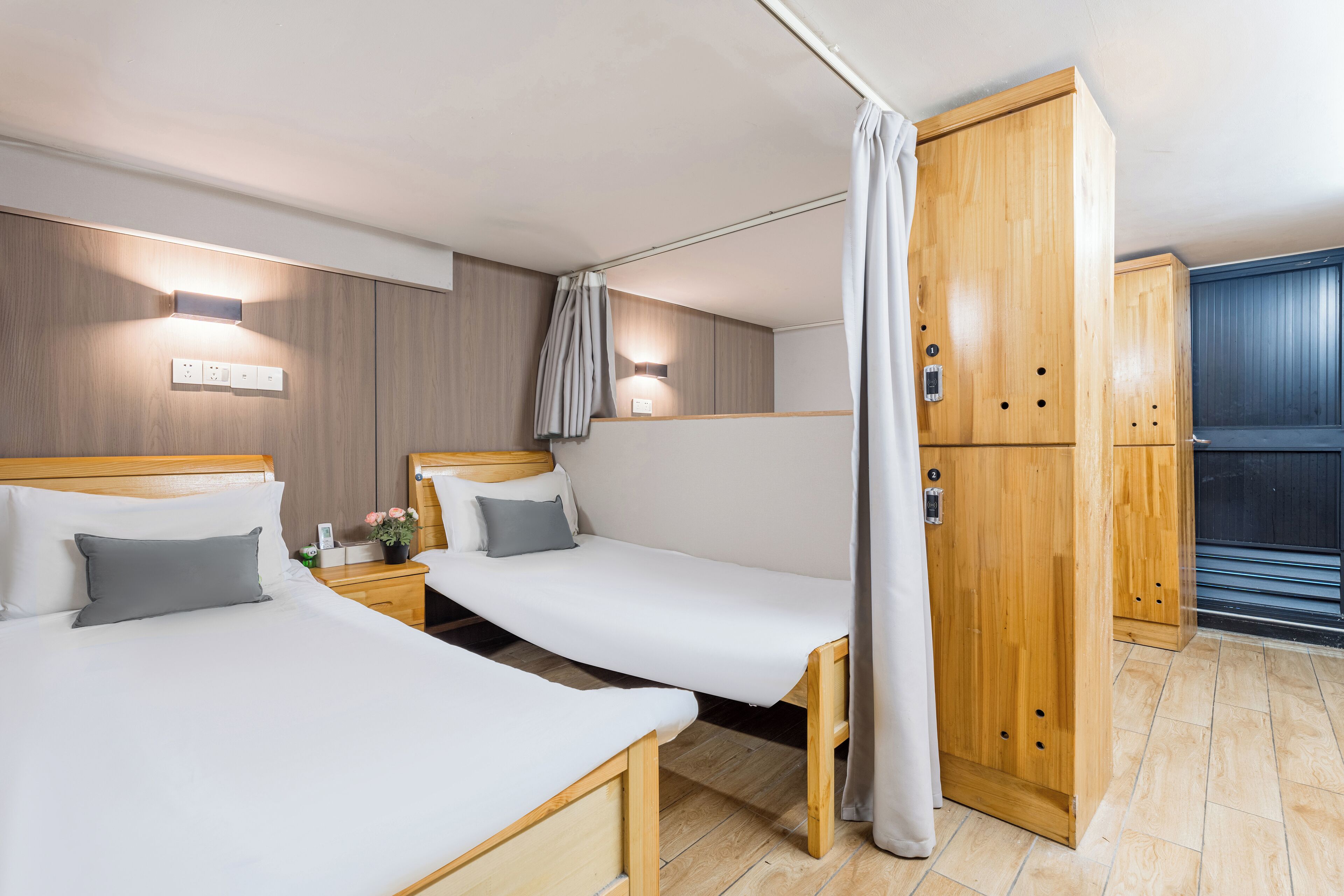 A hotel room with two single beds, wooden wardrobe, and a curtain.