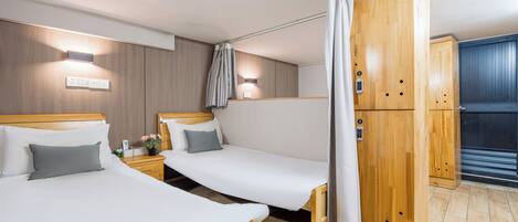 A hotel room with two single beds, wooden wardrobe, and a curtain.