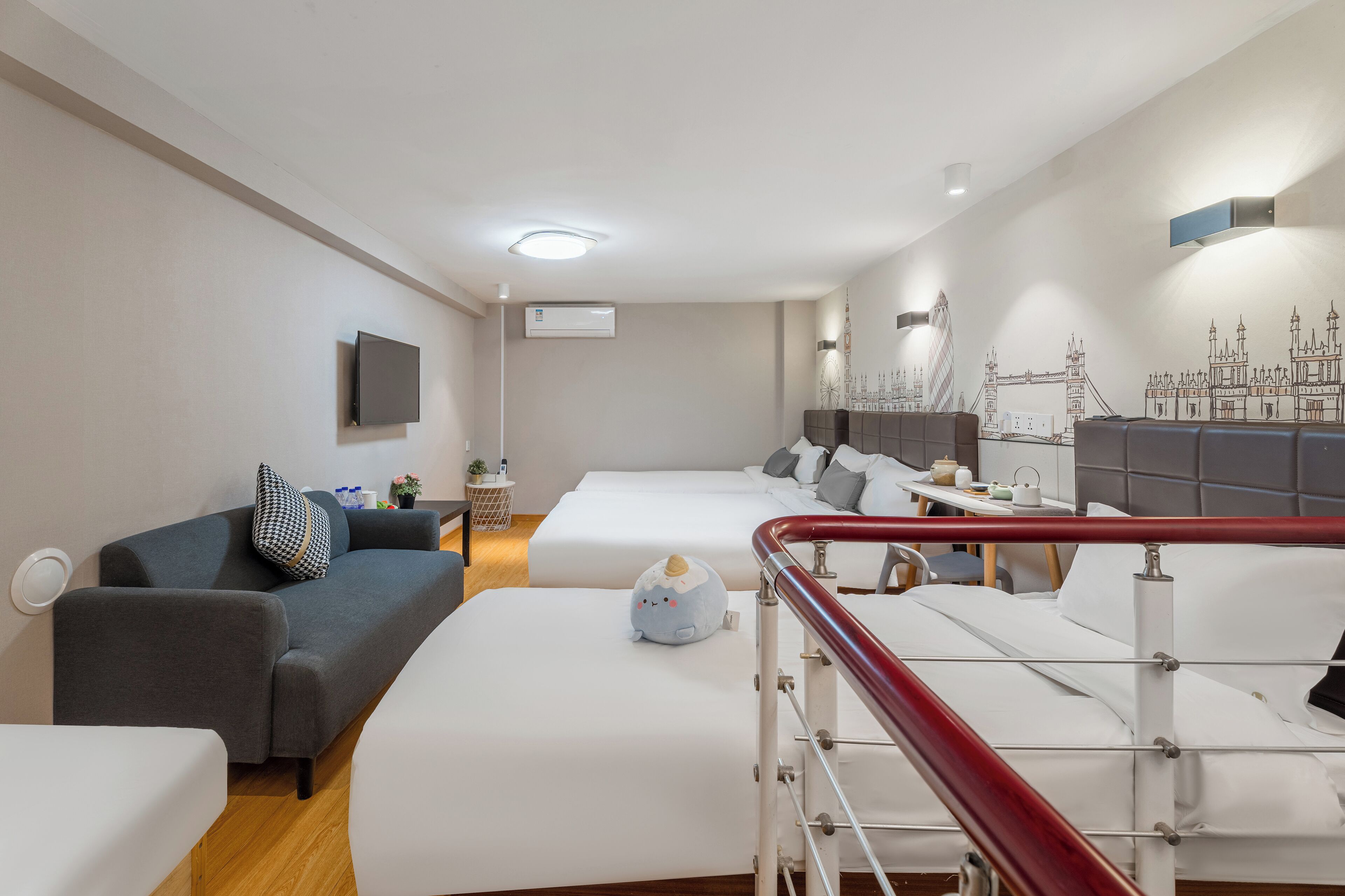 A modern hotel room with a sofa, two beds, a TV, and a mural of London landmarks.