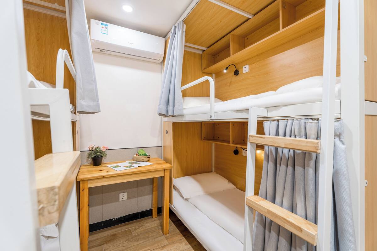 A compact, well-lit room with bunk beds, a small table with a plant, and a wooden desk.