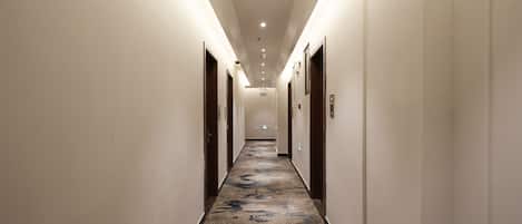 A long, narrow hallway with a patterned carpet, white walls, and doors on both sides.