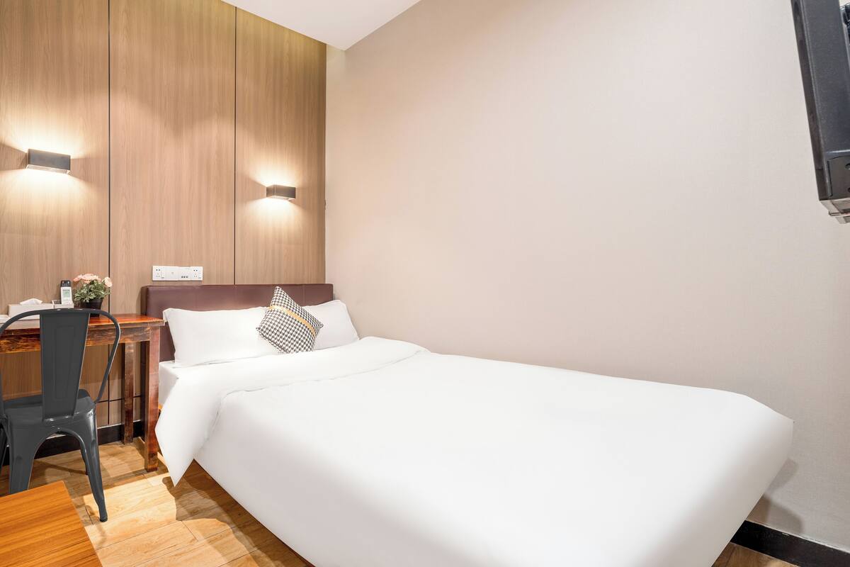A hotel room with a bed, a desk, a chair, and a wall-mounted TV.