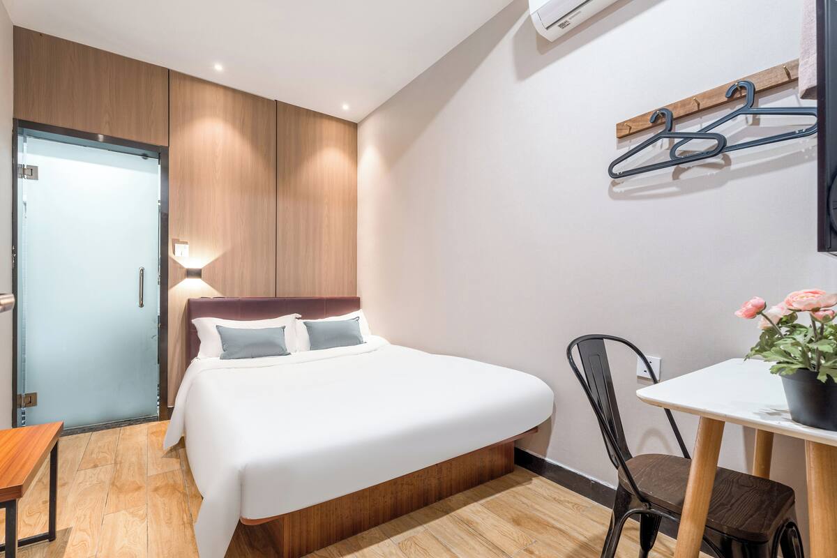 A hotel room with a bed, bedside table, chair, and a small table with a potted plant.