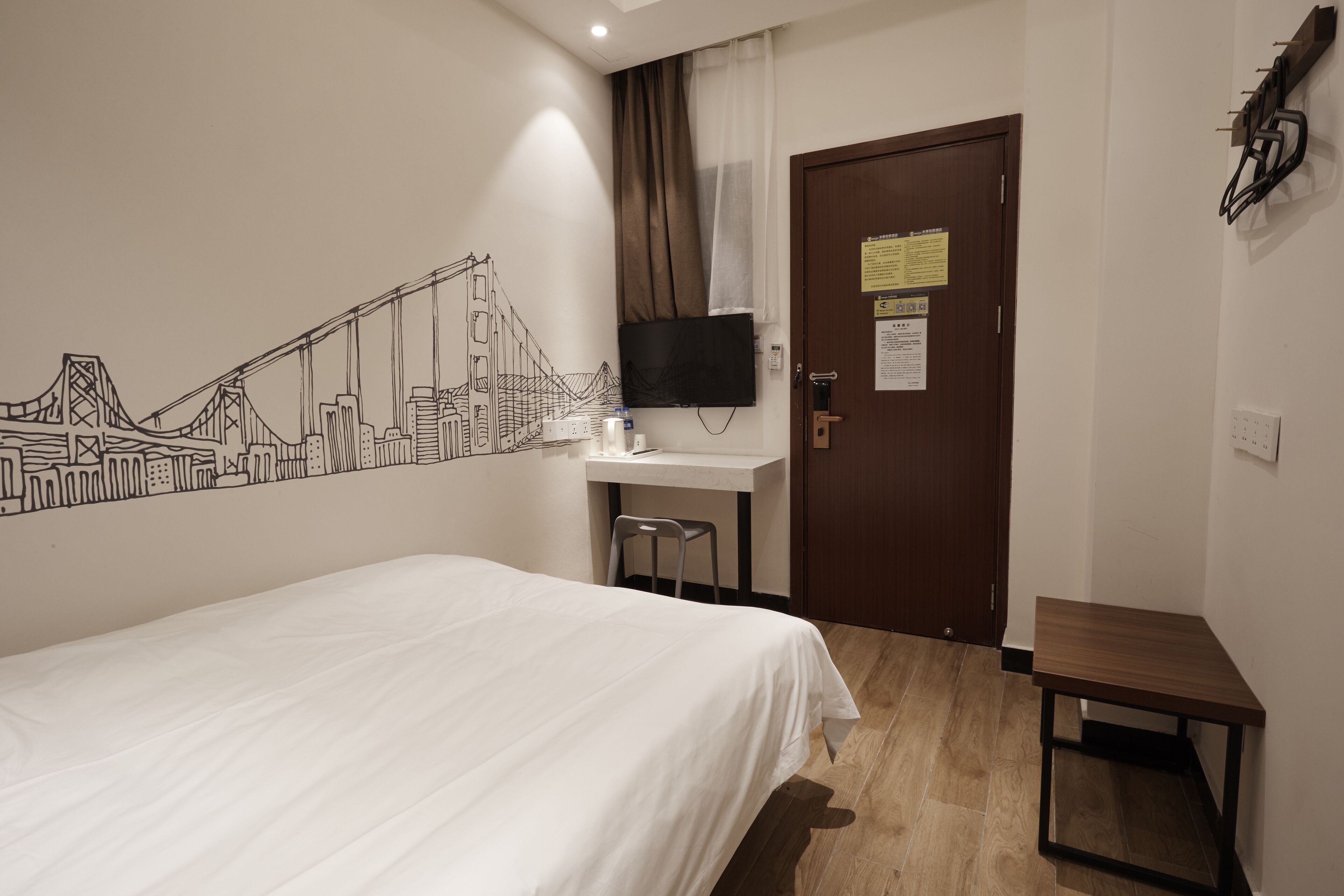 Een hotelkamer met een bed, een bureau met stoel, een aan de muur bevestigde televisie en een deur met een bordje.