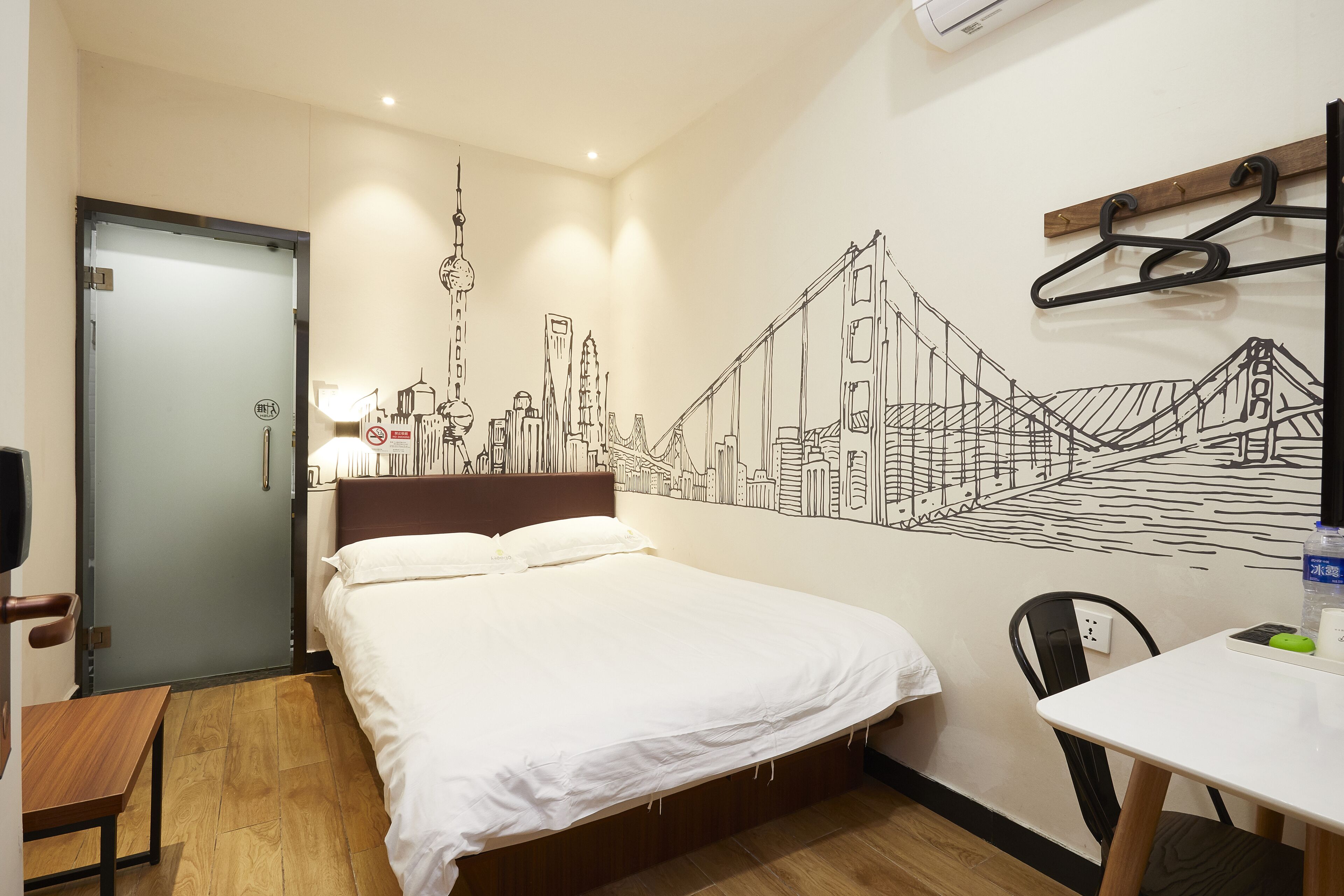 Una habitación de hotel con cama, escritorio, silla, un mural en la pared y una puerta.