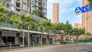 Un hotel moderno con fachada de vidrio, situado en una zona urbana con edificios altos al fondo.