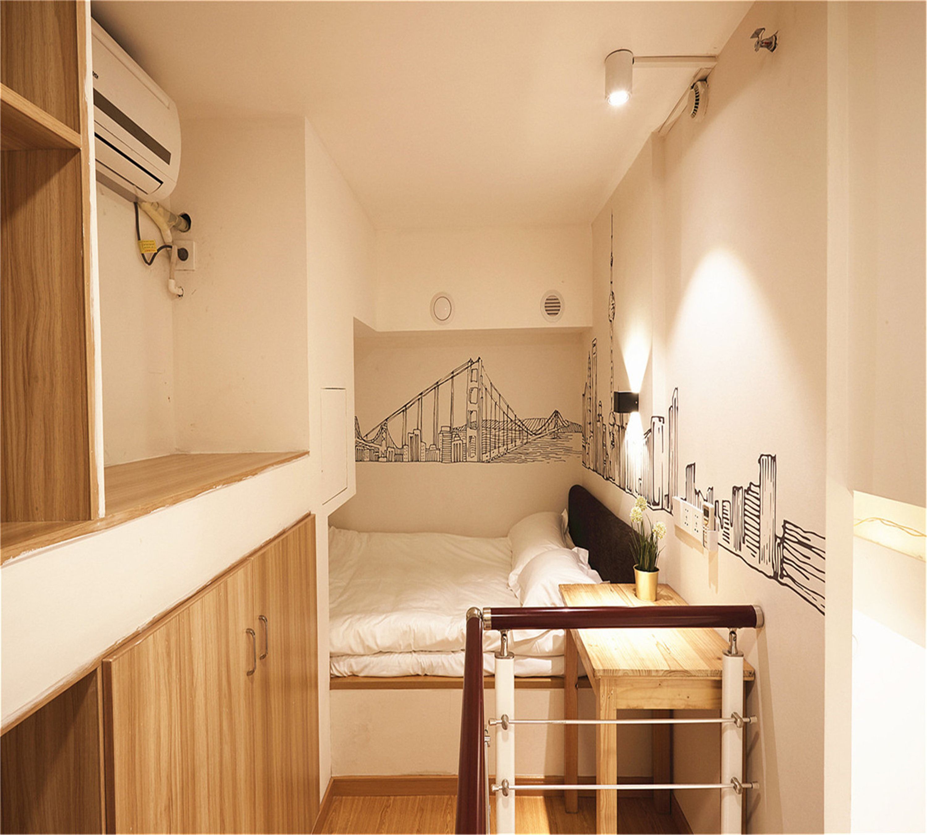 Ein kleines Zimmer mit Etagenbett, Holzschrank, Wandklimaanlage und Wandgemälde mit Stadtansicht.