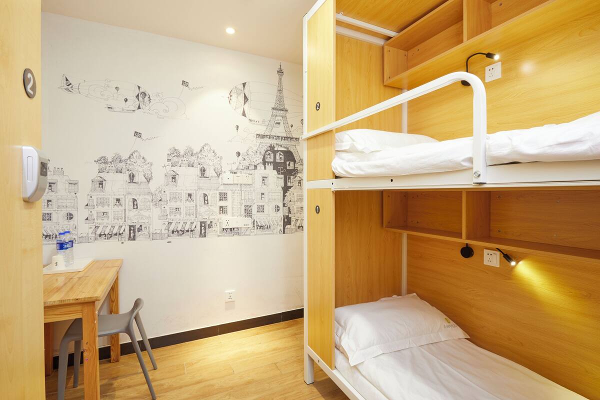 A bunk bed room with a wooden headboard, a desk with a chair, and a wall mural of Parisian scenes.