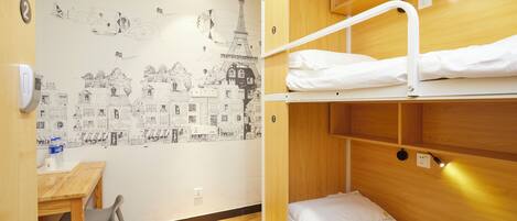 Habitación con literas, cabecera de madera, un escritorio con silla y un mural en la pared con escenas parisinas.
