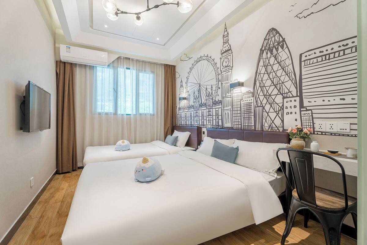 A hotel room with two beds, a flat-screen TV, a desk with a chair, and a mural of a city skyline.