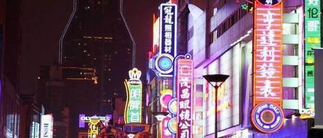 A brightly lit urban street at night with neon signs and illuminated buildings.