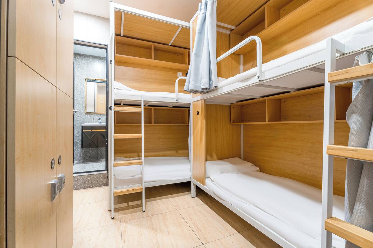 A bunk bed room with wooden bunk beds, a small bathroom with a mirror, and a wardrobe.
