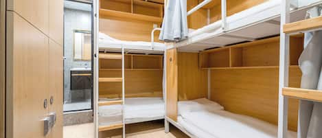 A bunk bed room with wooden bunk beds, a small bathroom with a mirror, and a wardrobe.