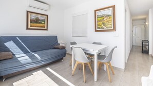 A modern living room with a blue sofa, a white dining table with chairs, and two framed landscape paintings on the wall. - Bacana 3-3 (Benidorm)