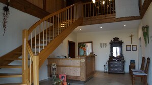 A spacious living area with a wooden staircase, a reception desk, and a dining area. - Kramerhof (Taufkirchen)