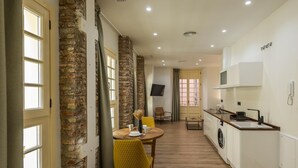 A compact kitchen with a washing machine, a dining area with a yellow chair, and a stone wall. - Chinitas 17 IIi - iloftmalaga (Málaga)