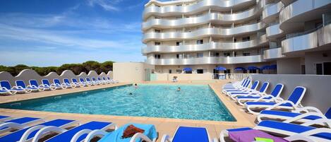 A swimming pool with lounge chairs and a multi-story building in the background.