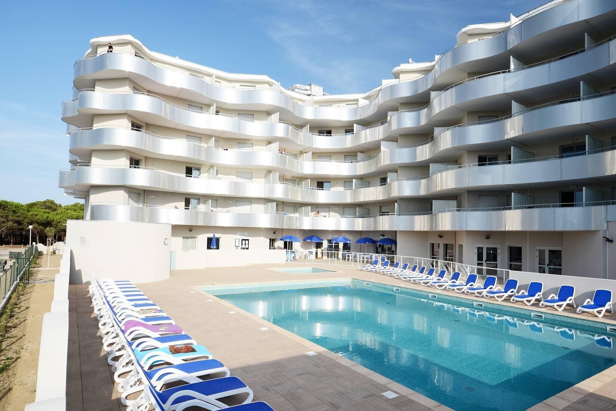 A multi-story hotel with a swimming pool and sun loungers.