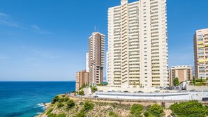 A high-rise hotel with multiple floors, located near a coastline with a clear blue sky.