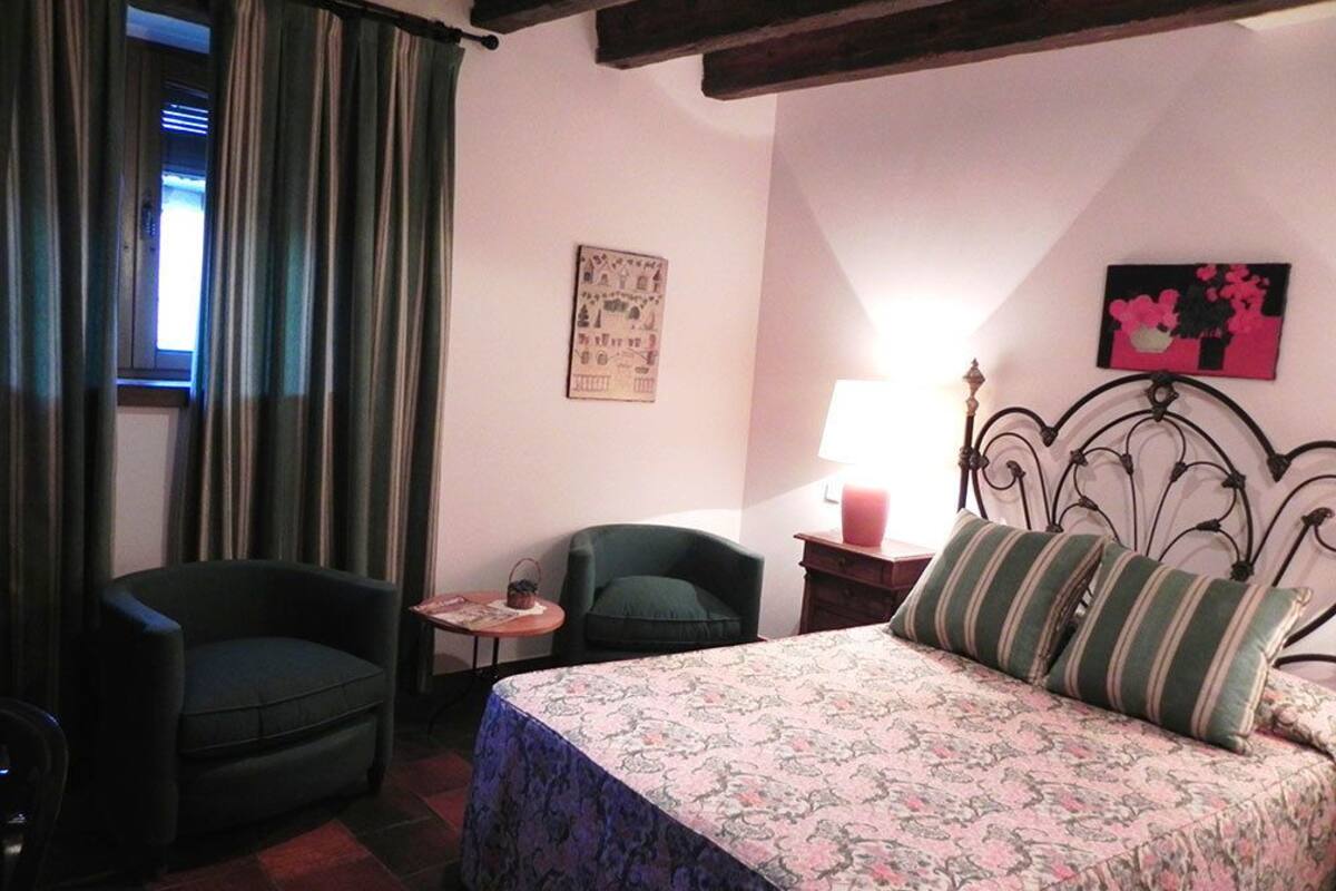A bedroom with a bed, a chair, a small table, a lamp, and curtains.