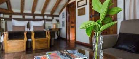 A room with a wooden ceiling, a sofa, a table with magazines, and a vase with green leaves.